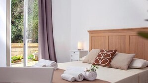 Hotellihuone, jossa on sänky, yöpöytä, lamppu ja näkymä vihreälle alueelle.