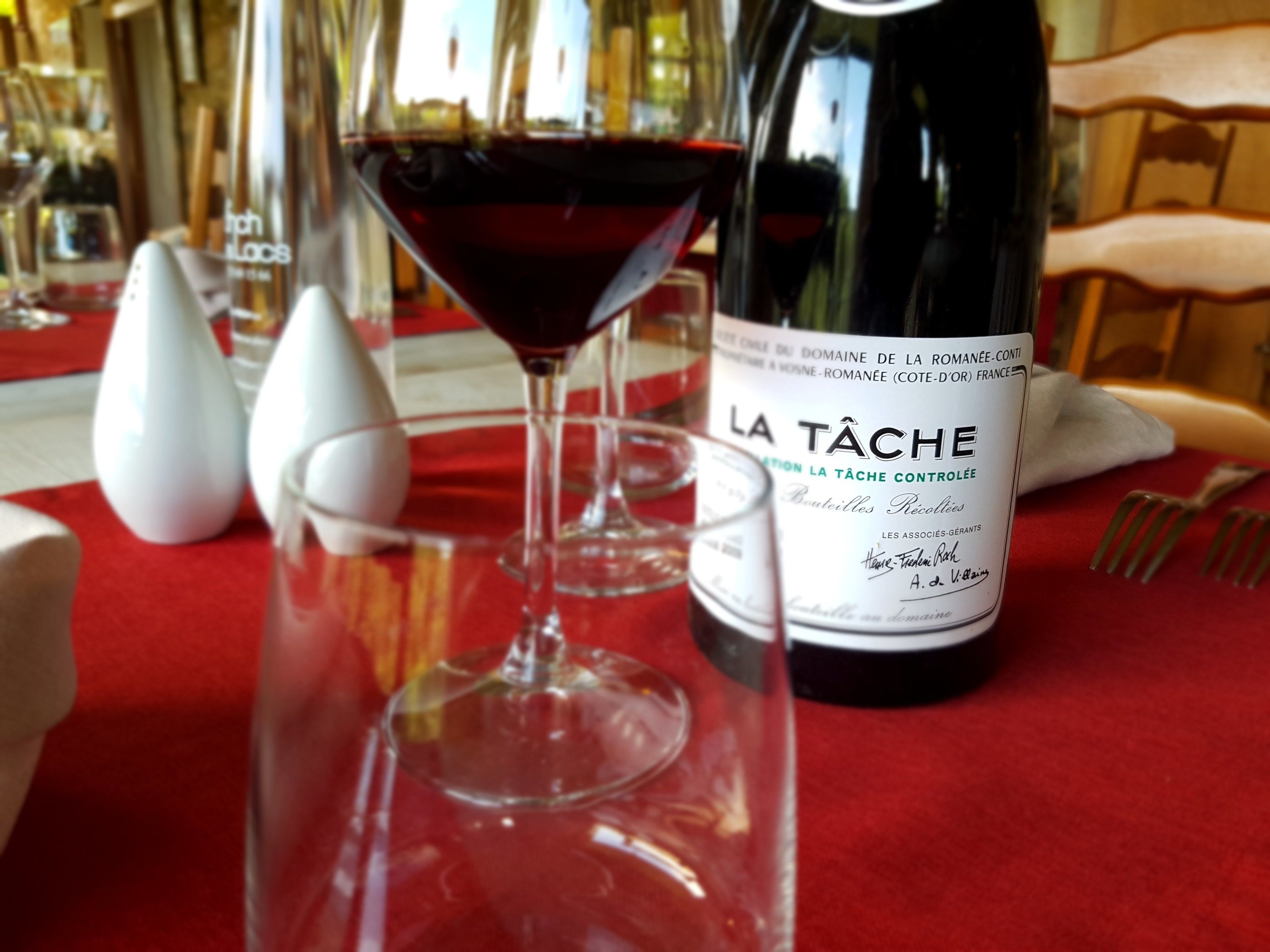 A wine bottle and a glass of red wine on a table with a red tablecloth.