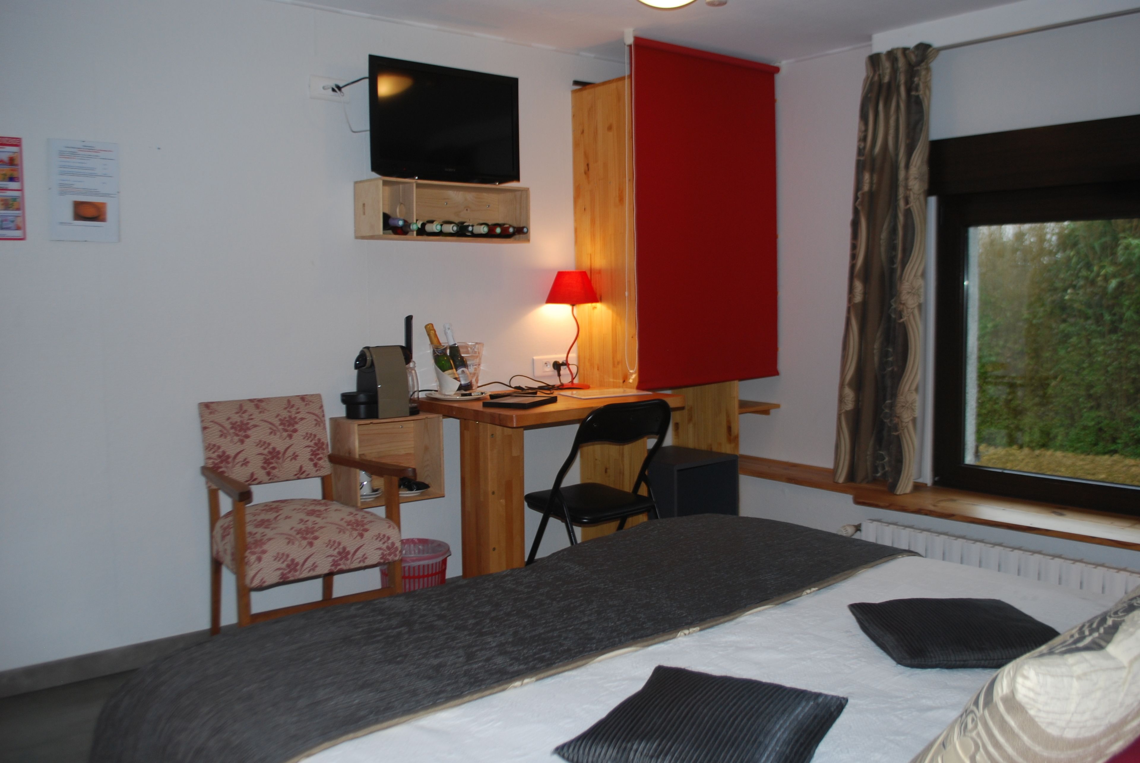 A bedroom with a bed, a desk with a computer, a chair, a TV mounted on the wall, and a window with curtains.