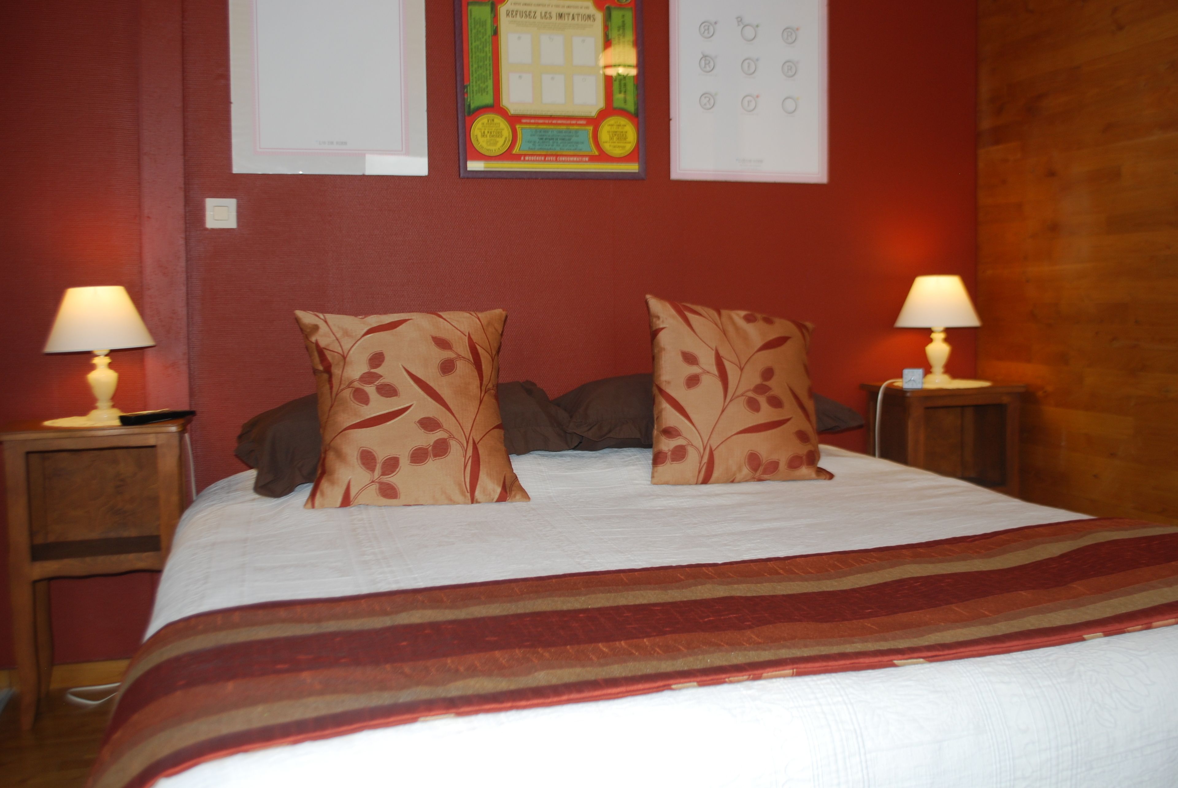 Un lit bien fait, agrémenté de deux coussins décoratifs, un mur rouge et deux lampes de chevet.