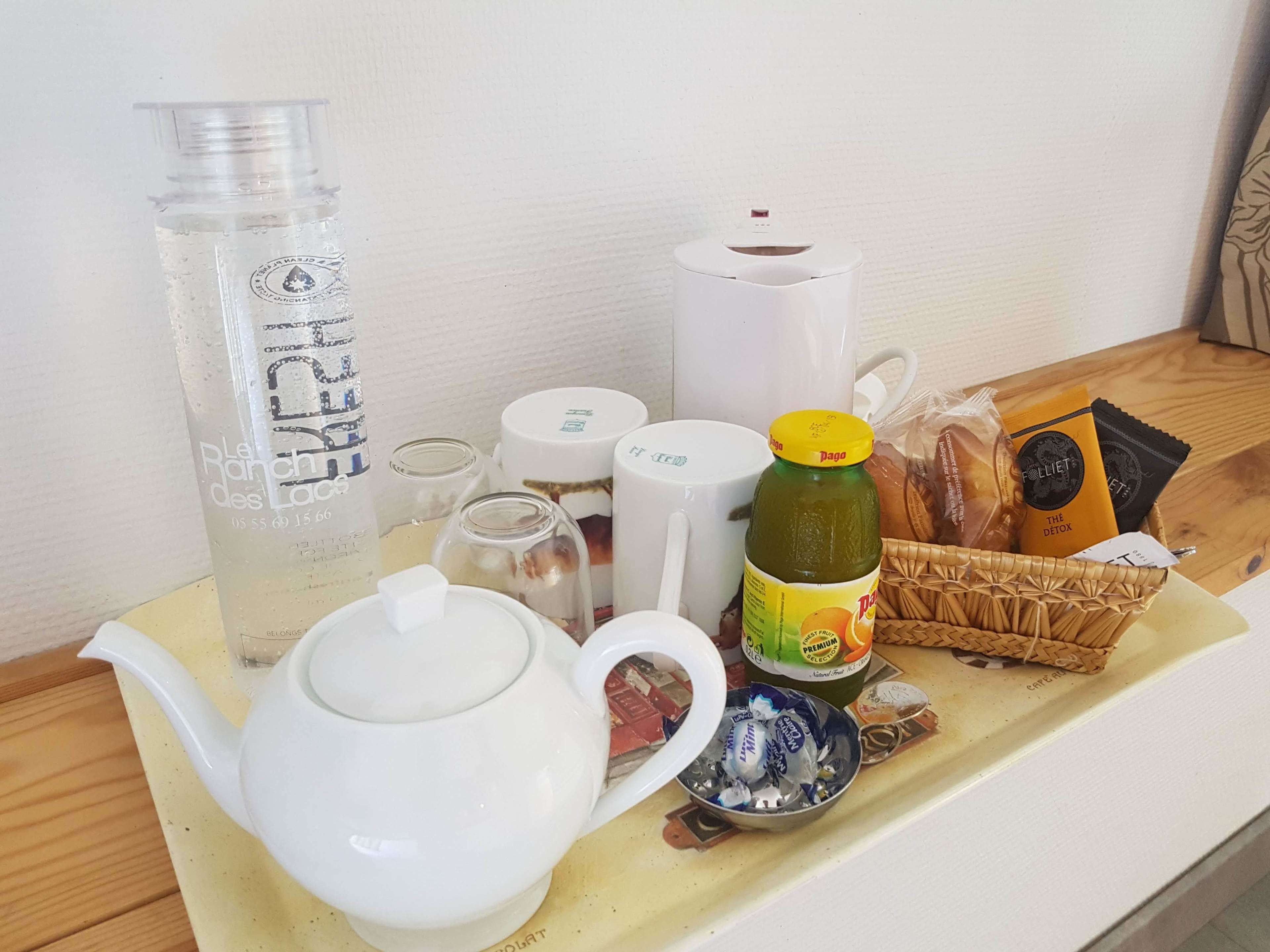 A table with a teapot, a bottle of juice, a basket of snacks, and a mug.
