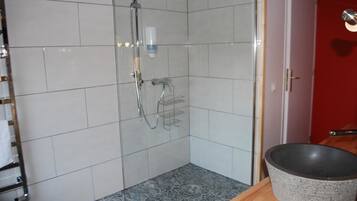 Et badeværelse med hvide flisemure, en bruser med håndbruser, en sæbedispenser og en stor vask på en træbordplade.