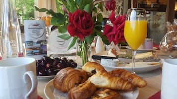 Una mesa de desayuno con croissants, cerezas, un vaso de jugo de naranja y un florero con rosas rojas.