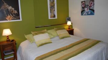 A neatly made bed with a striped bedspread, two bedside lamps, and three framed artworks on the walls.