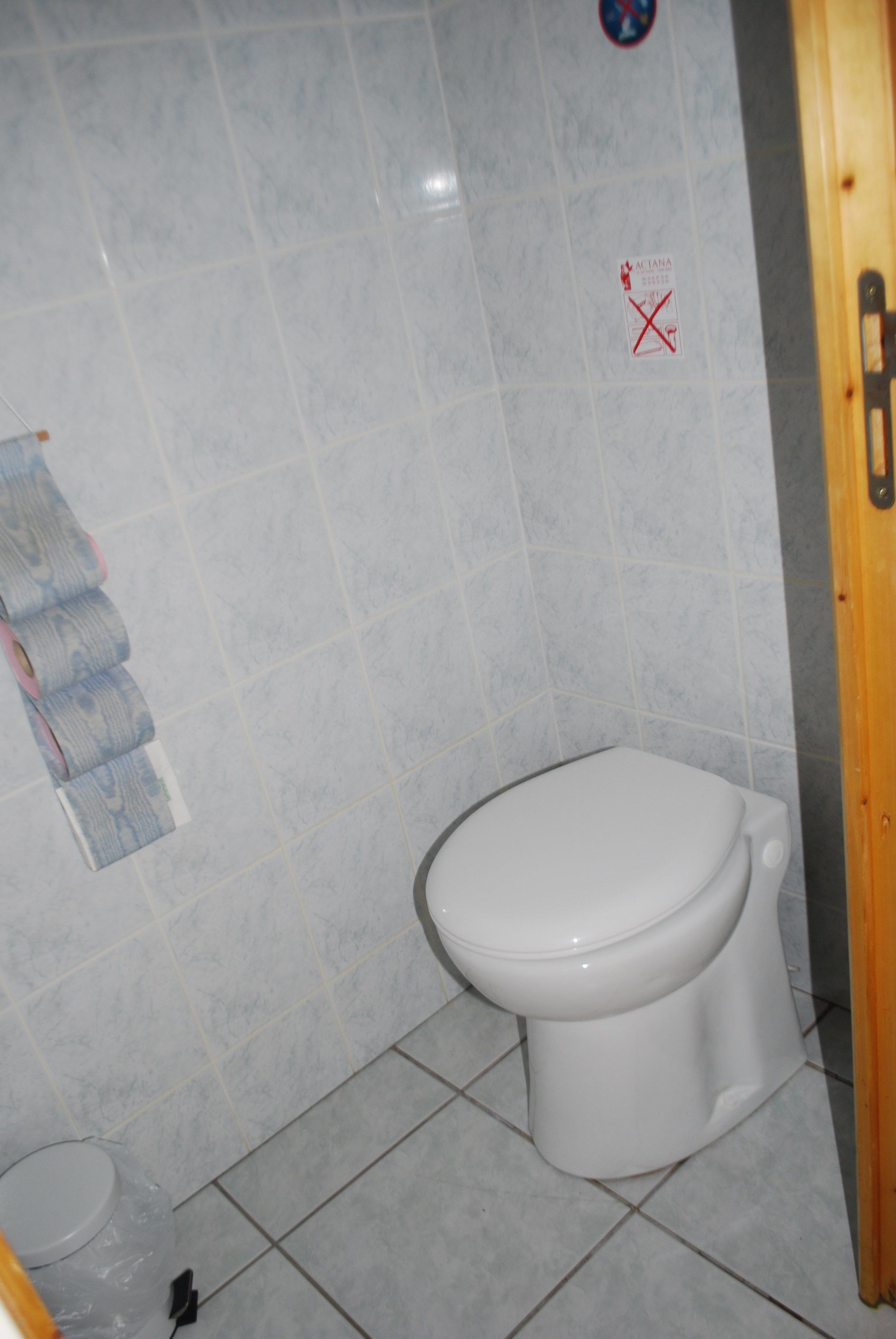 Ein Badezimmer mit Toilette, gefliesten Wänden und einer Holztür.