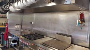 A commercial kitchen with stainless steel surfaces, a gas stove, and hanging pots. - Le Ranch des Lacs, Hôtel Restaurant à Augne (Augne)