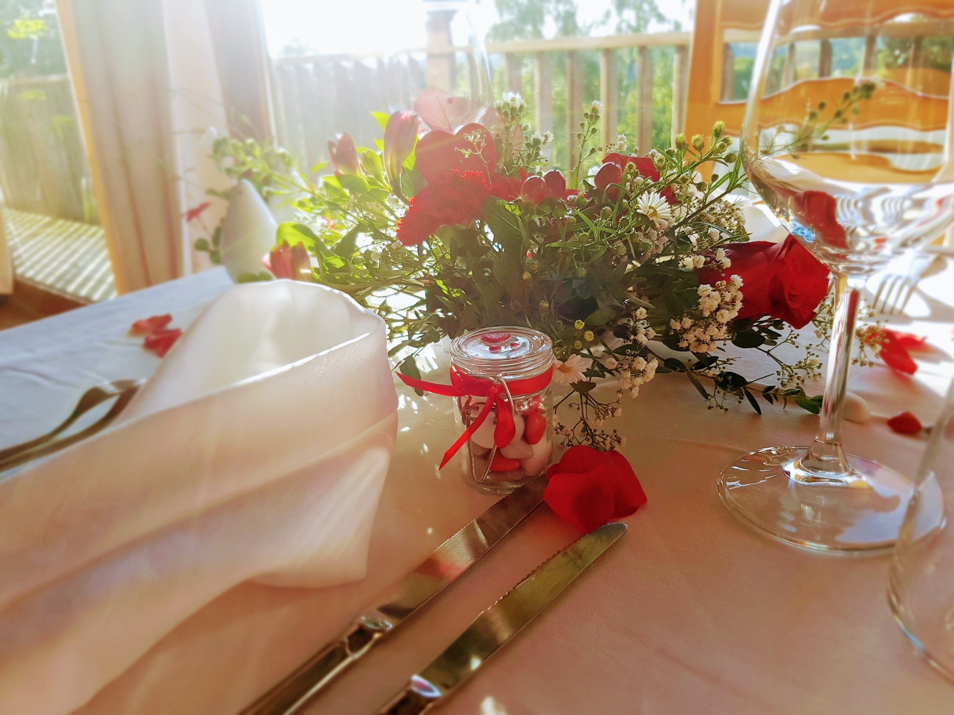 Ein Tisch, gedeckt für eine Mahlzeit, mit einer Glasvase als Mittelpunkt, einer roten Rose und einem Weinglas.