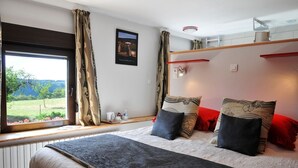 A bedroom with a large bed, a window with curtains, a bedside table with a lamp, and a wall-mounted shelf. - Le Ranch des Lacs, Hôtel Restaurant à Augne (Augne)
