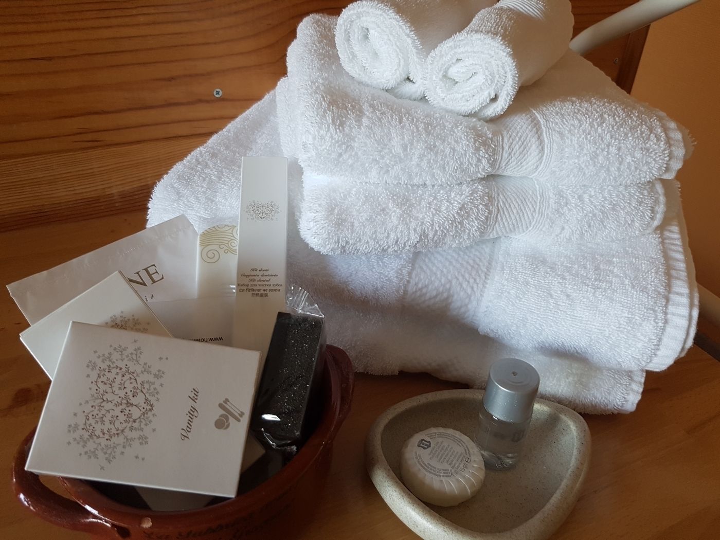 A wooden table with a white towel, a bath kit, and a bottle of soap.
