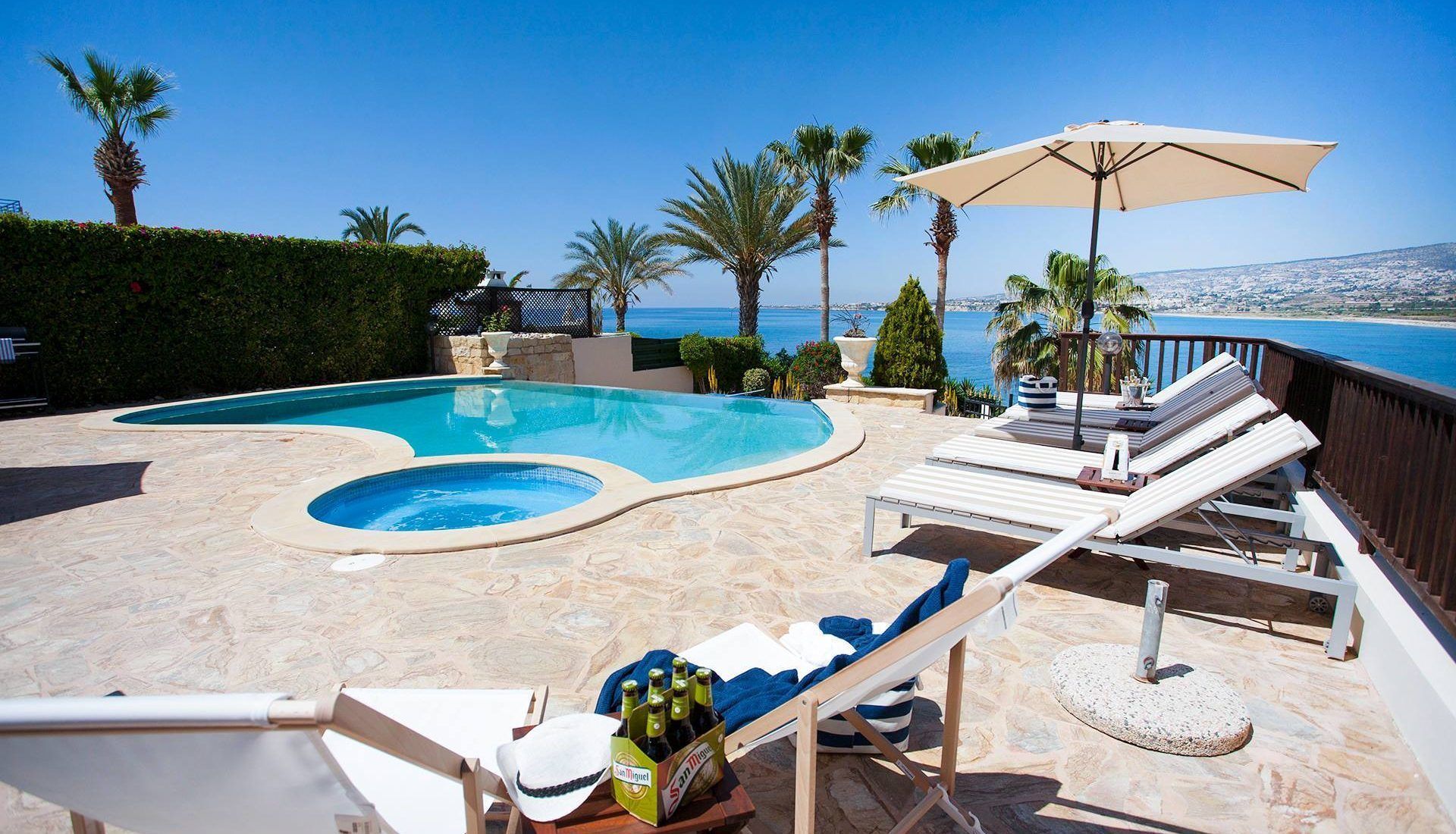 A pool area with two hot tubs, lounge chairs, and a view of the sea.