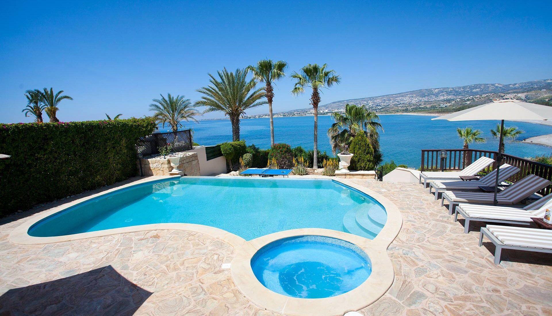 Una piscina con jacuzzi, sillas de descanso y palmeras con vistas a la costa.