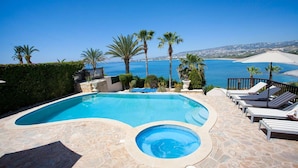 Una piscina con jacuzzi, sillas de descanso y palmeras con vistas a la costa.