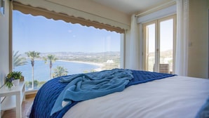 Un dormitorio con cama, vistas al mar y un balcón con una planta.