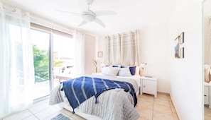 Un dormitorio con cama, mesita de noche, ventilador de techo y vistas al exterior.