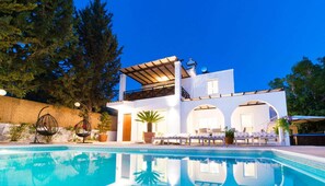Una casa moderna de dos pisos con piscina, mobiliario exterior y una pérgola.