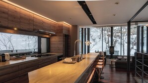 Una cocina moderna con una isla grande, taburetes de bar y vistas a árboles a través de amplios ventanales.