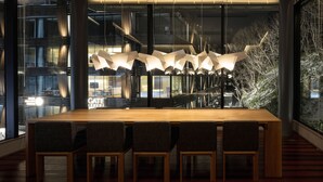 Un área de comedor moderna con una mesa y sillas de madera, ventanas amplias con vistas a la ciudad y una lámpara de techo original.