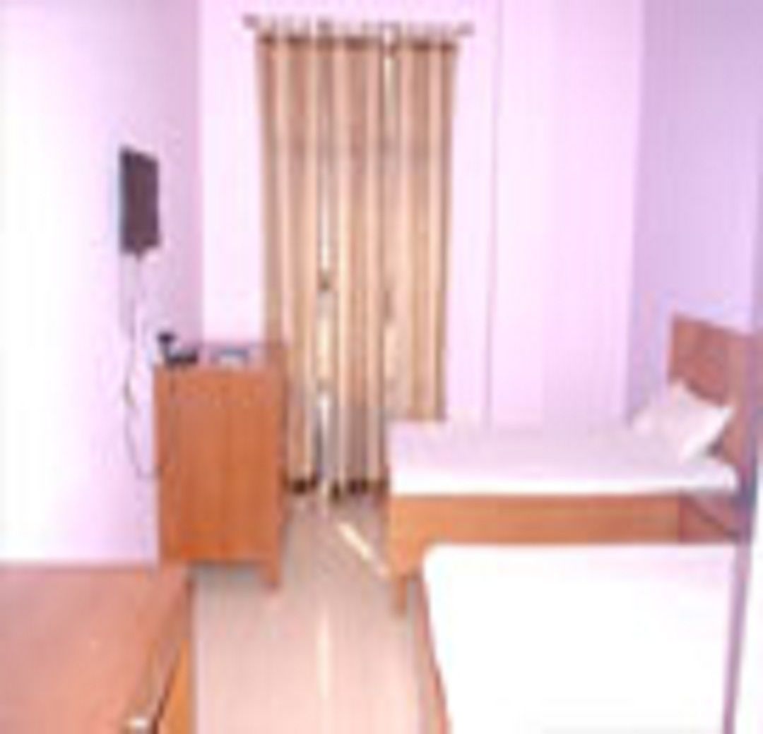 A small, simple room with a bed, a wooden dresser, and a curtain.