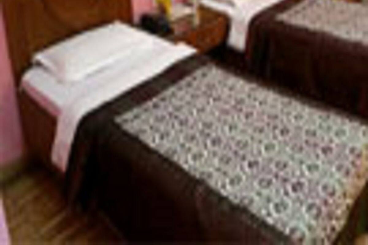 A room with two single beds, wooden headboards, a nightstand with a lamp, and a small table with a bottle.