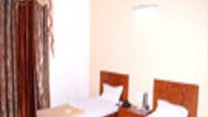 A hotel room with two single beds, a nightstand, a lamp, and a window with curtains.