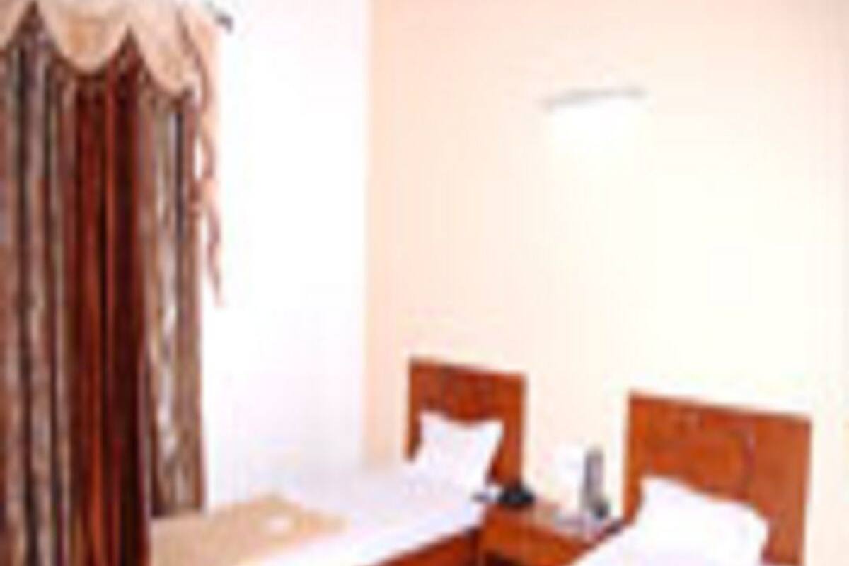 A hotel room with two single beds, a nightstand, a lamp, and a window with curtains.