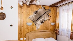 A room with a wooden headboard, a bed with white bedding, a dining table with chairs, and a wall-mounted light fixture. - Grunyk Guest House (Yaremche)