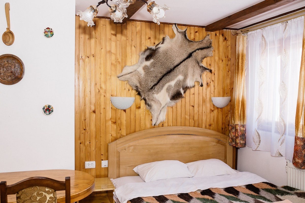 A room with a wooden headboard, a bed with white bedding, a dining table with chairs, and a wall-mounted light fixture.
