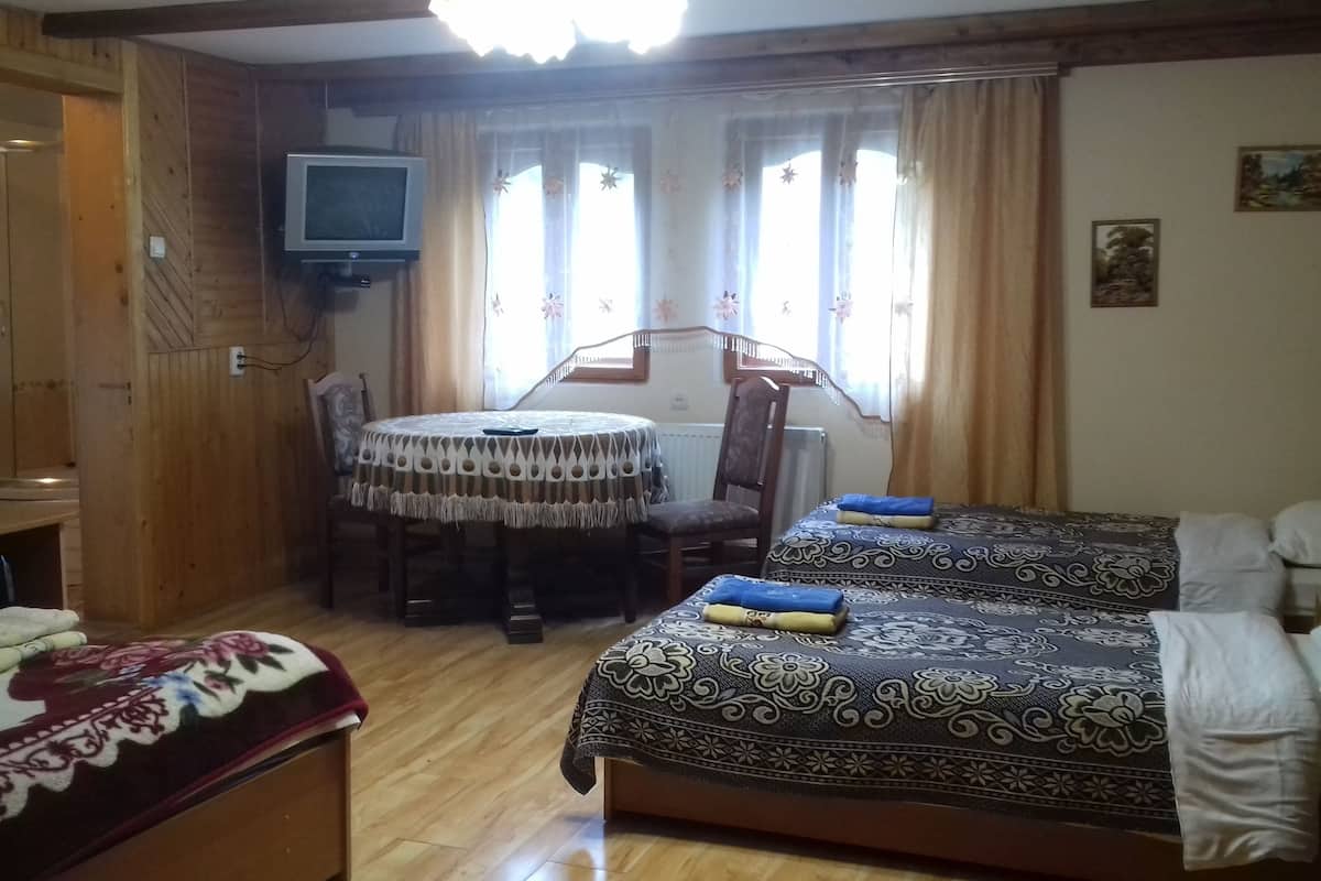 A room with two beds, a dining table with chairs, a television, and a window with curtains.