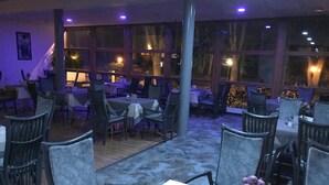 An indoor dining area with tables and chairs, large windows, and a staircase. - Hotel Aquarius (Braunschweig)