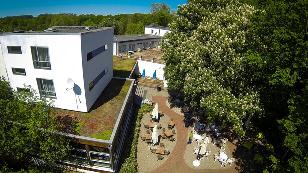 A modern building with a flat roof, outdoor seating area, and a large tree. - Hotel Aquarius (Braunschweig)