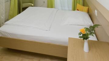 A neatly made bed with a white mattress and a wooden headboard. There is a green chair and a small table with a vase of flowers.