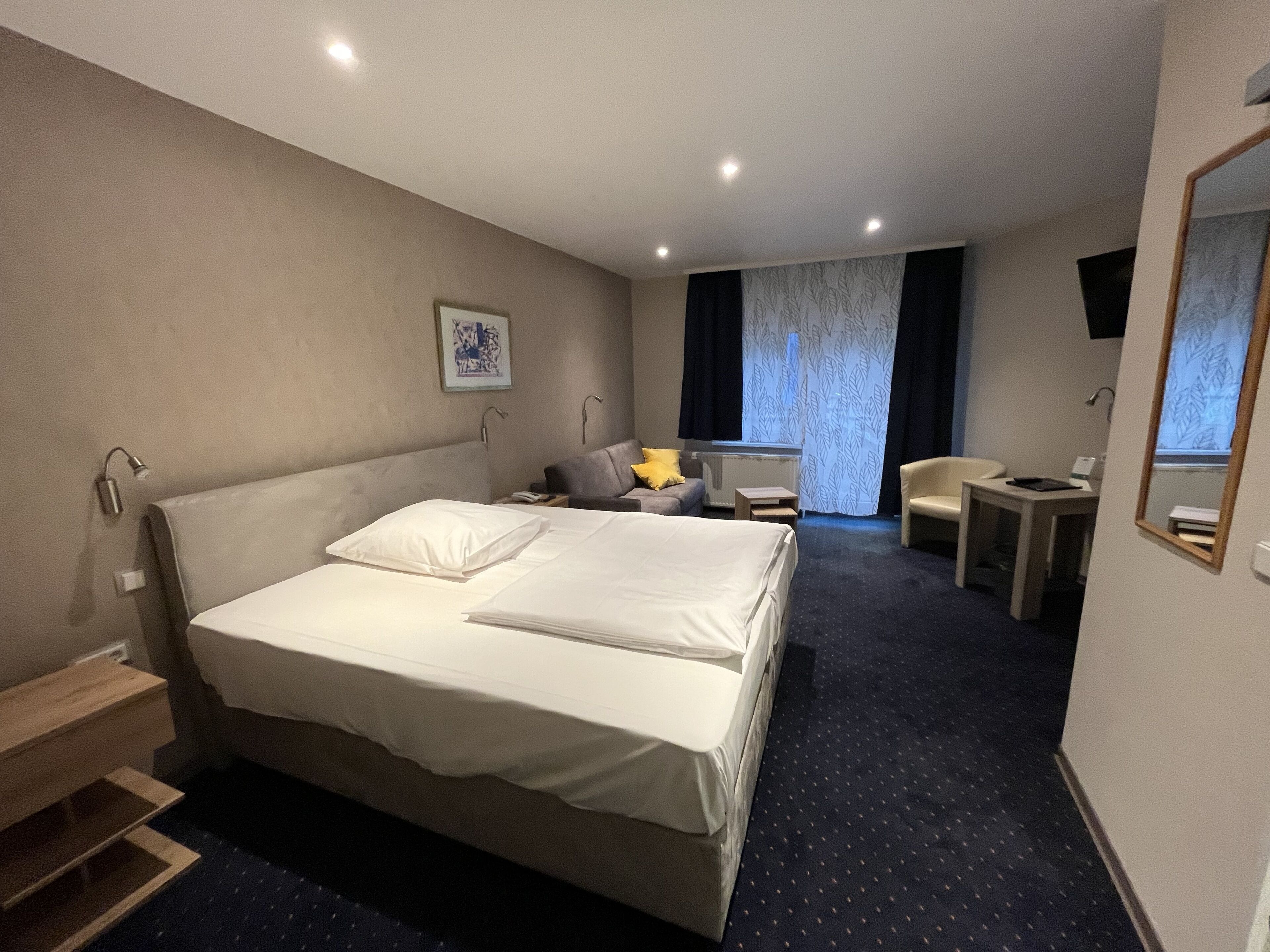 Een hotelkamer met een groot bed, een klein bureau, een stoel en een raam met gordijnen.