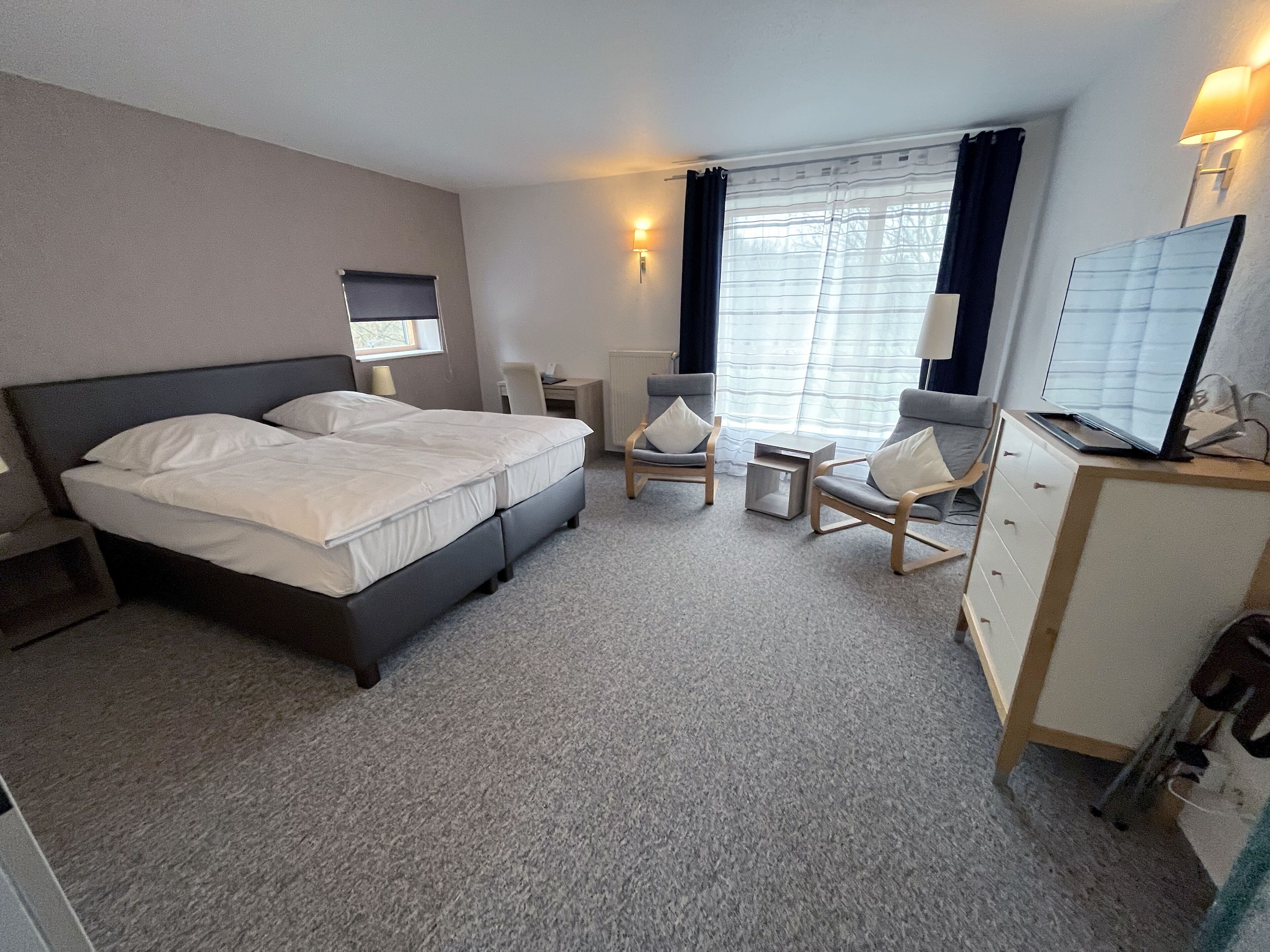 A hotel room with a double bed, two armchairs, a desk, a dresser, and a TV on the dresser.
