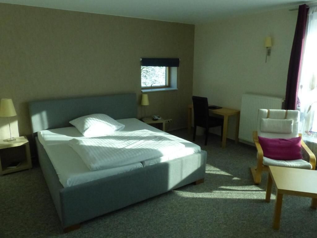 Habitació d'hotel amb llit, escriptori, cadira, finestra i làmpada.