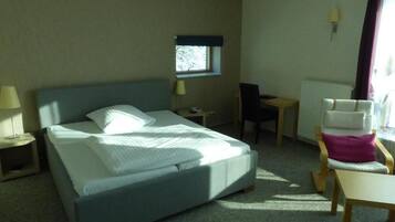 Habitació d'hotel amb llit, escriptori, cadira, finestra i làmpada.