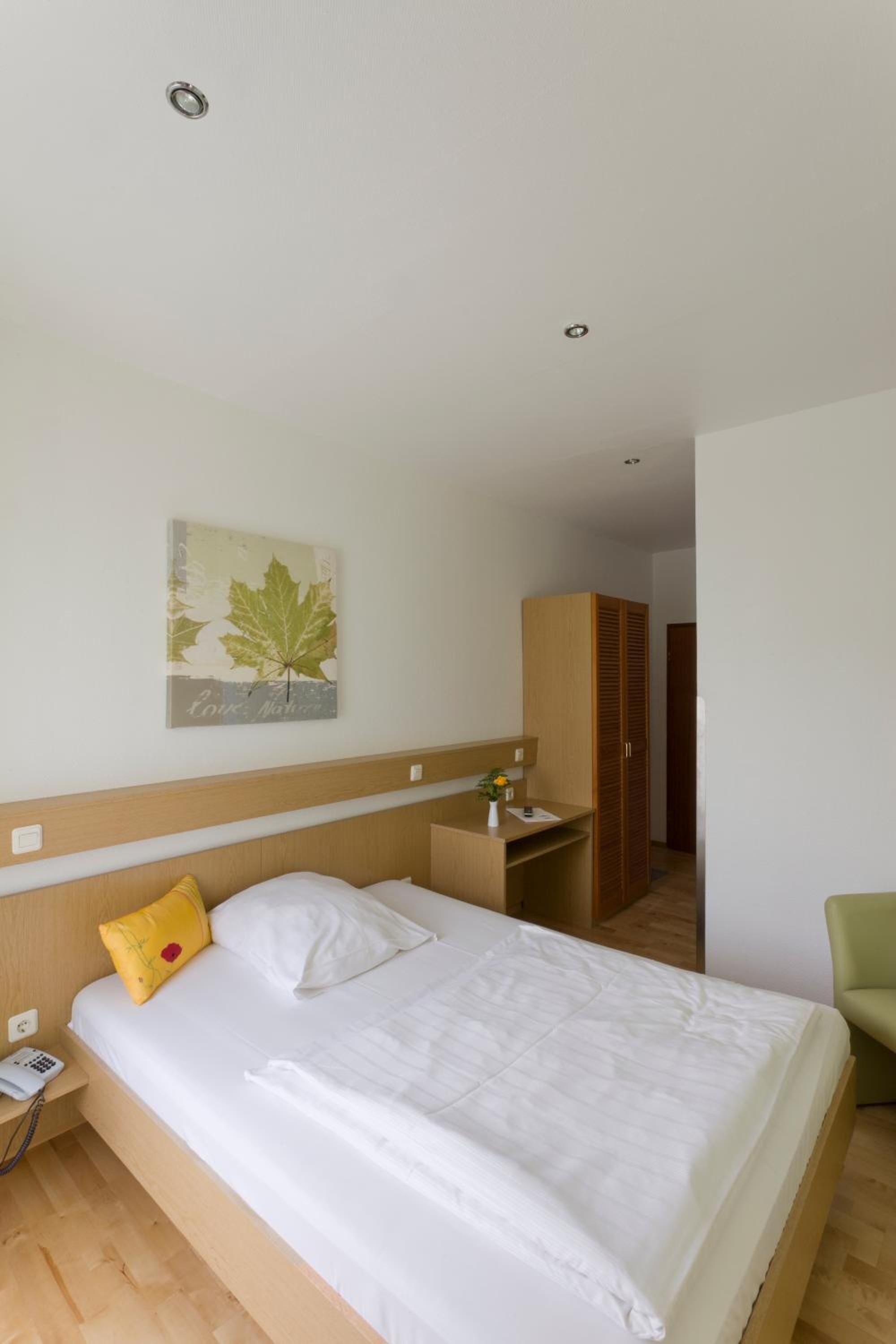 Een hotelkamer met een bed, een nachtkastje met een lamp, een telefoon, een kledingkast en een schilderij aan de muur.