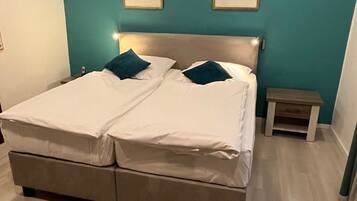 A double bed with white linens and two pillows, a wooden nightstand, and two framed pictures on teal walls.