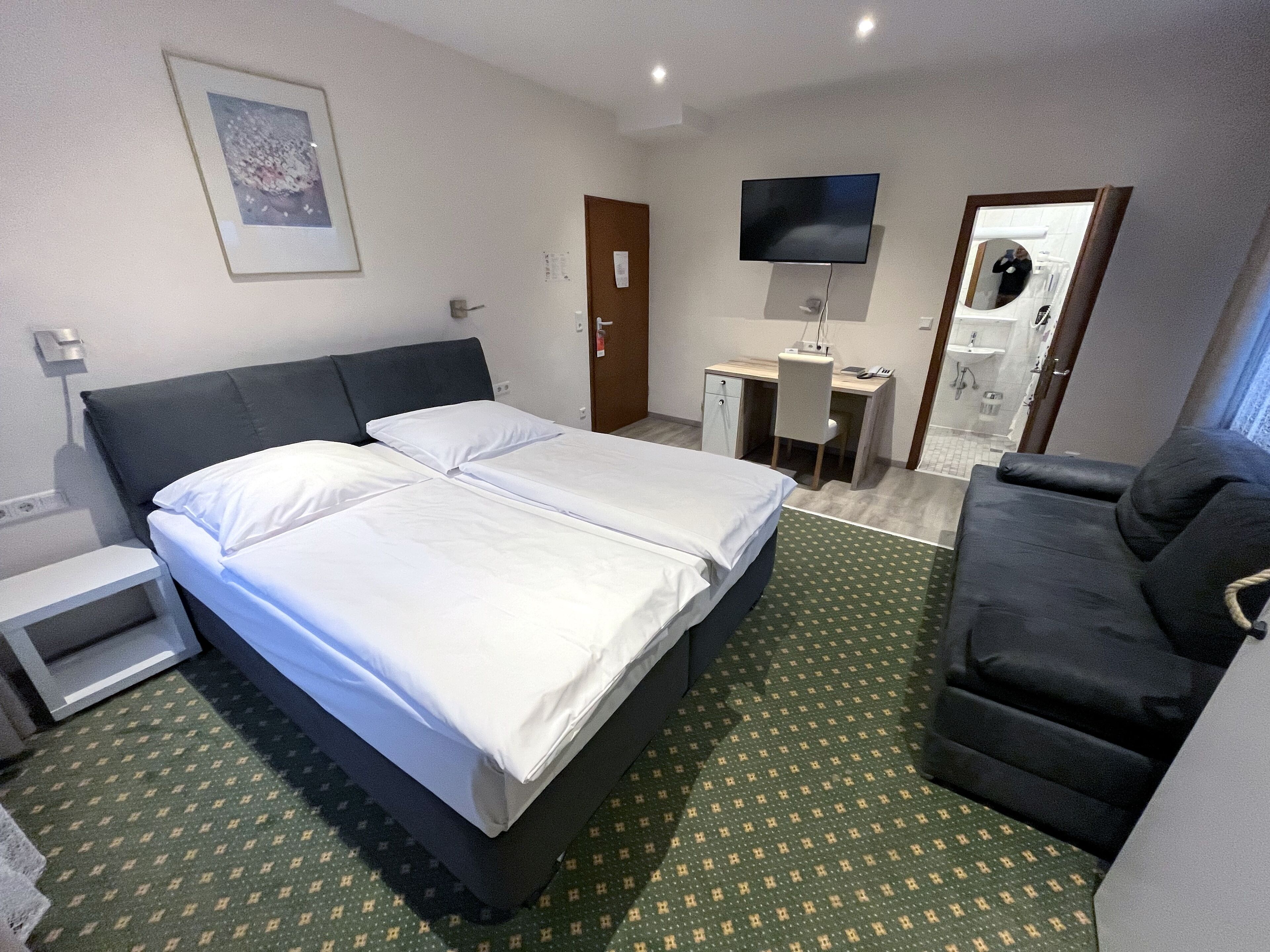 Ein Hotelzimmer mit Bett, Schreibtisch, Stuhl, Fernseher und einem durchgegangenen Tür sichtbaren Badezimmer.