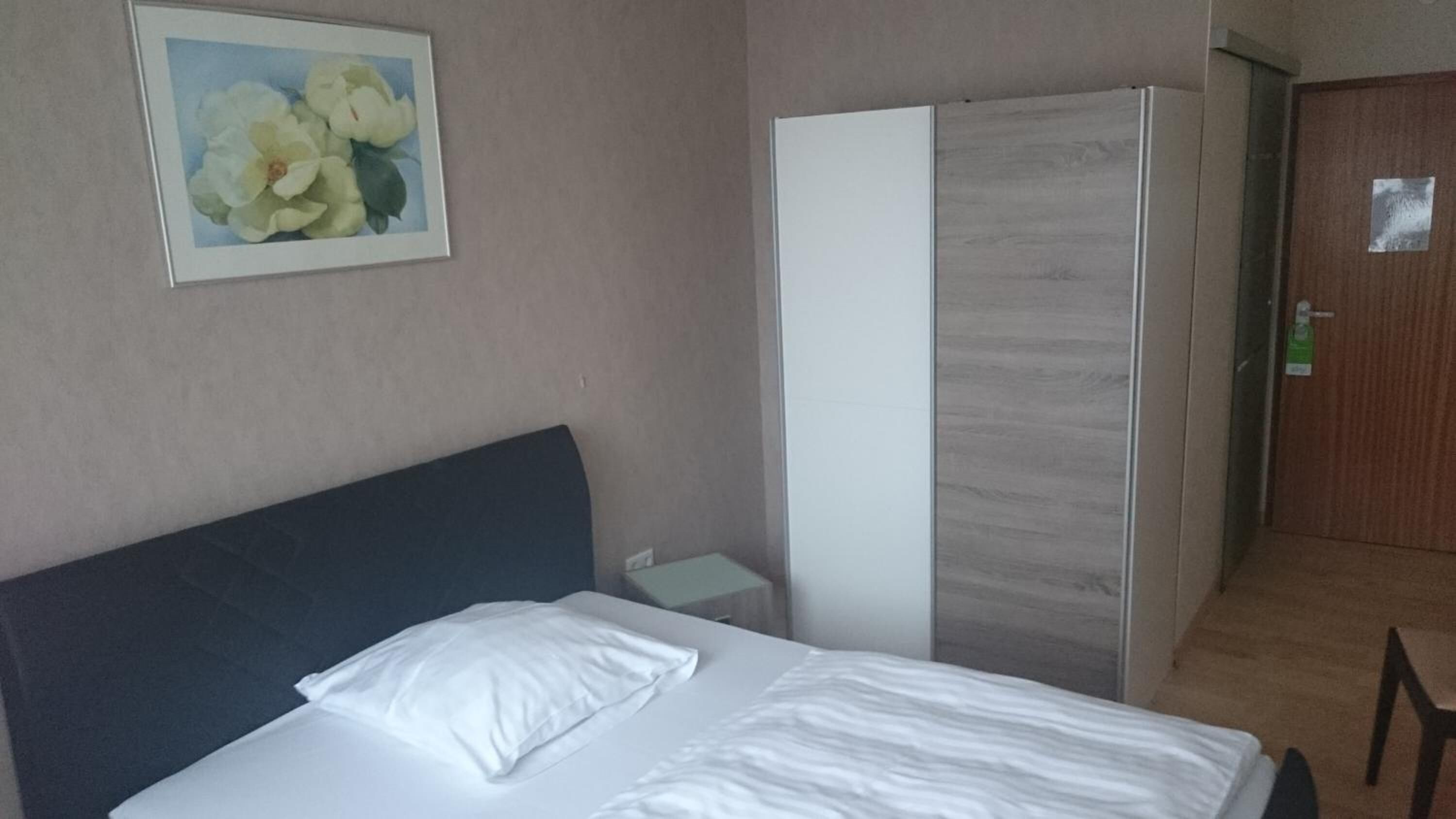 A hotel room with a bed, a nightstand, a wardrobe, and a door.