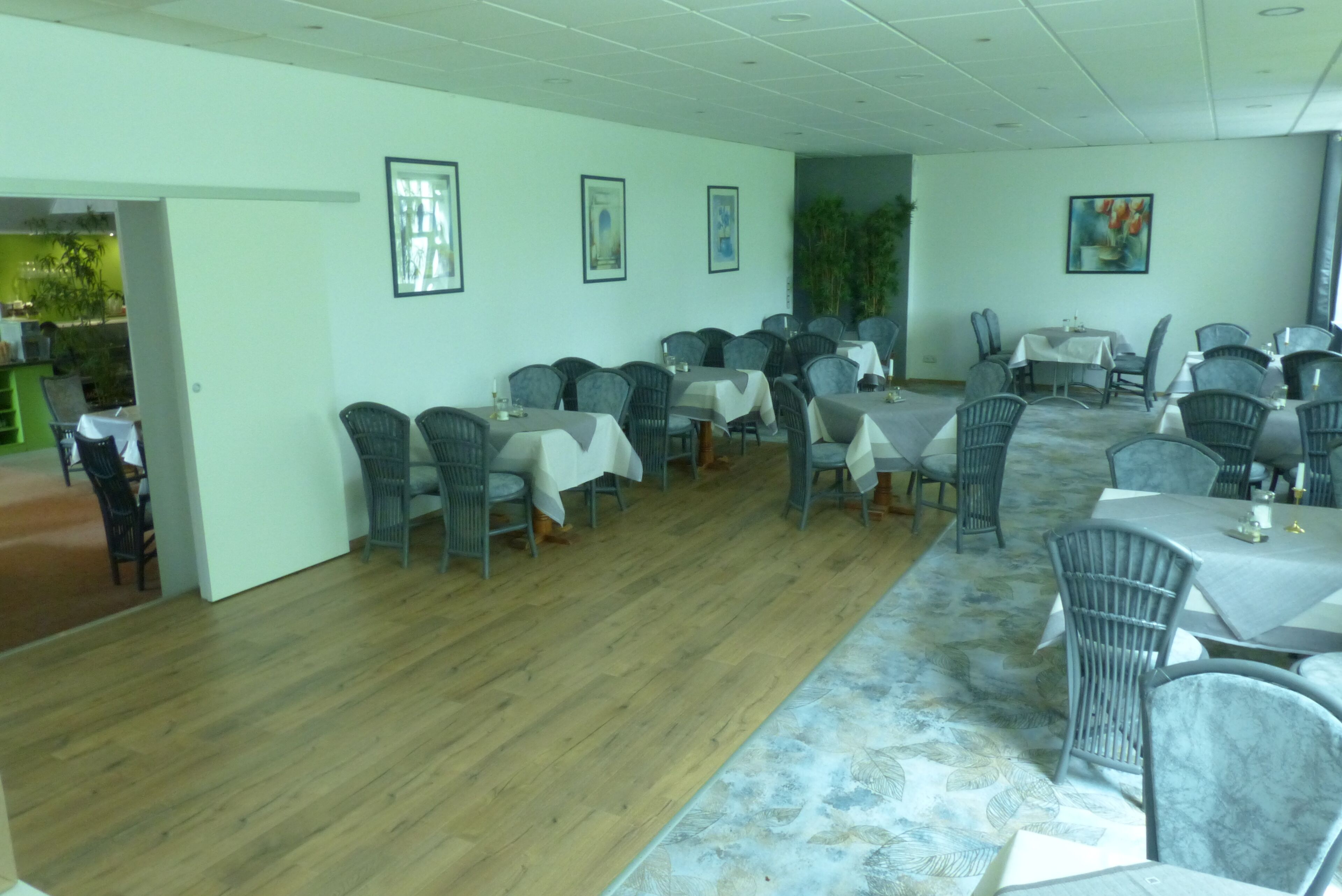 A dining area with multiple tables and chairs, wooden flooring, and framed artwork on the walls.