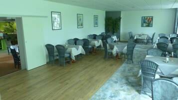 A dining area with multiple tables and chairs, wooden flooring, and framed artwork on the walls.
