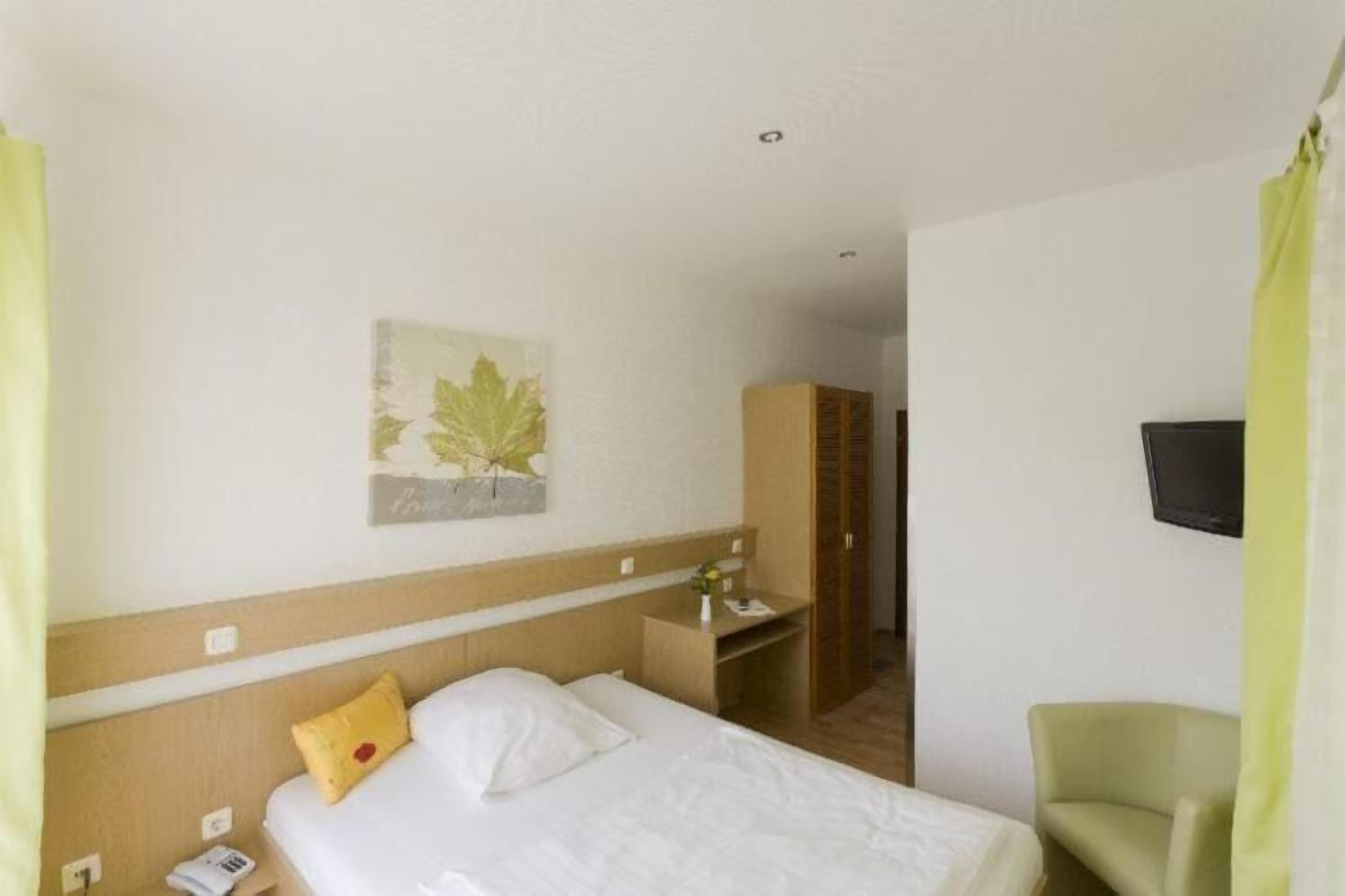 A hotel room with a bed, a desk, a chair, a television, and a wardrobe.