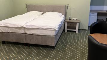 Et hotelværelse med en dobbeltseng, et lille natbord med telefon, en stol og et grønt mønstret tæppe.