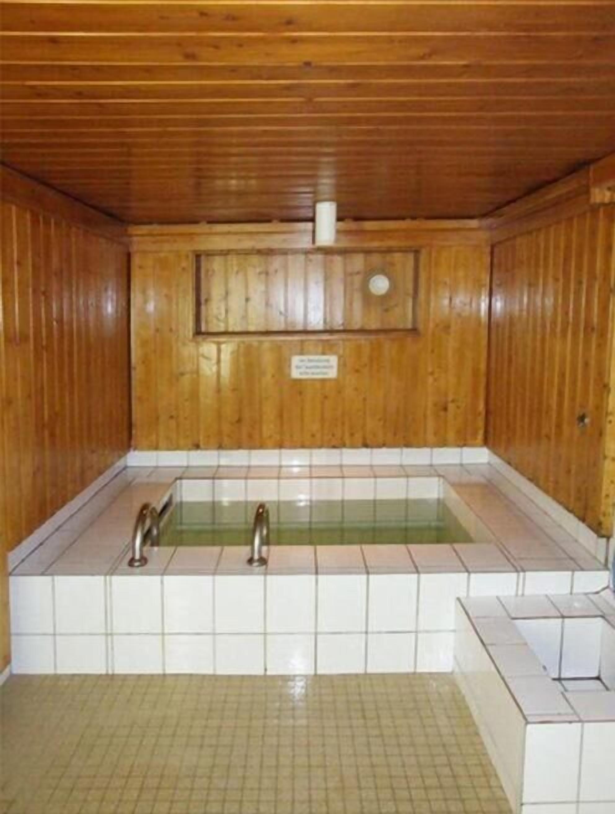 Una sauna de madera con piso de baldosas y dos grifos.