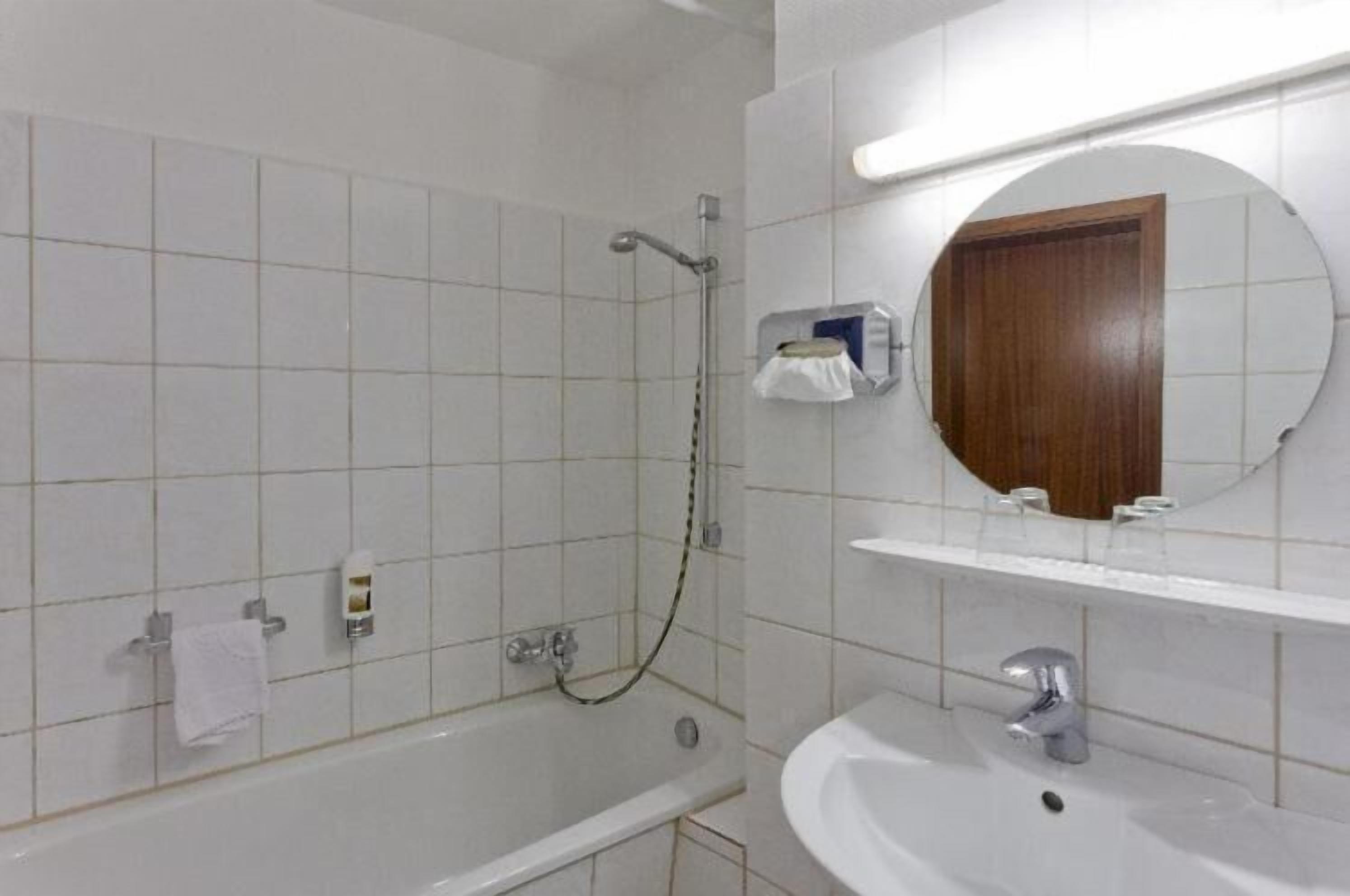 A bathroom with white tiles, a bathtub, a shower, a sink, a mirror, and a towel rack.