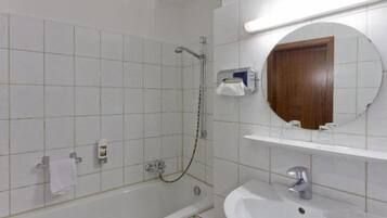 A bathroom with white tiles, a bathtub, a shower, a sink, a mirror, and a towel rack.