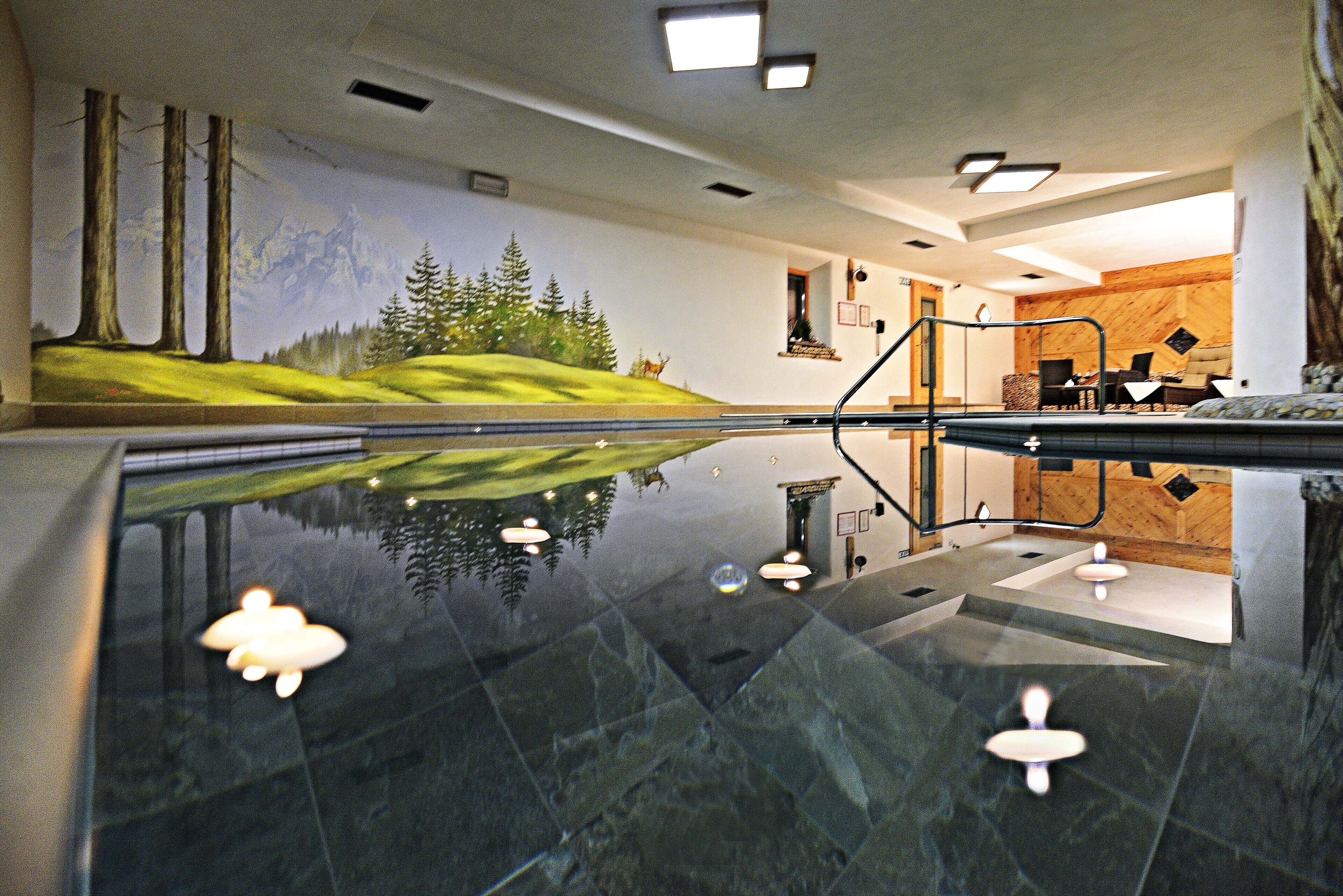Una piscina interior moderna con superficie reflectante, un mural de paisaje montañoso y diseño interior en madera.