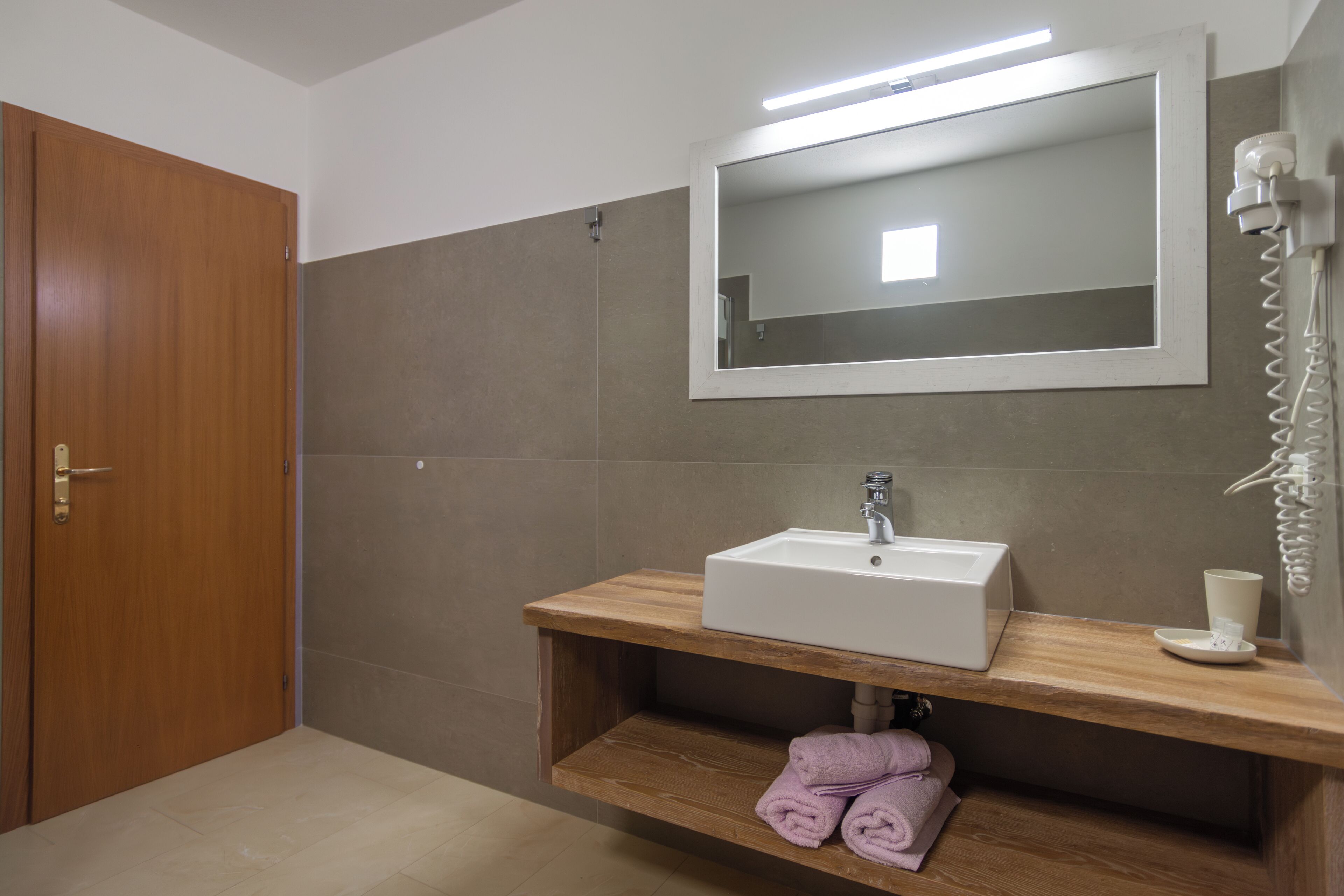A bathroom with a wooden vanity, a white sink, a mirror, and a hairdryer.