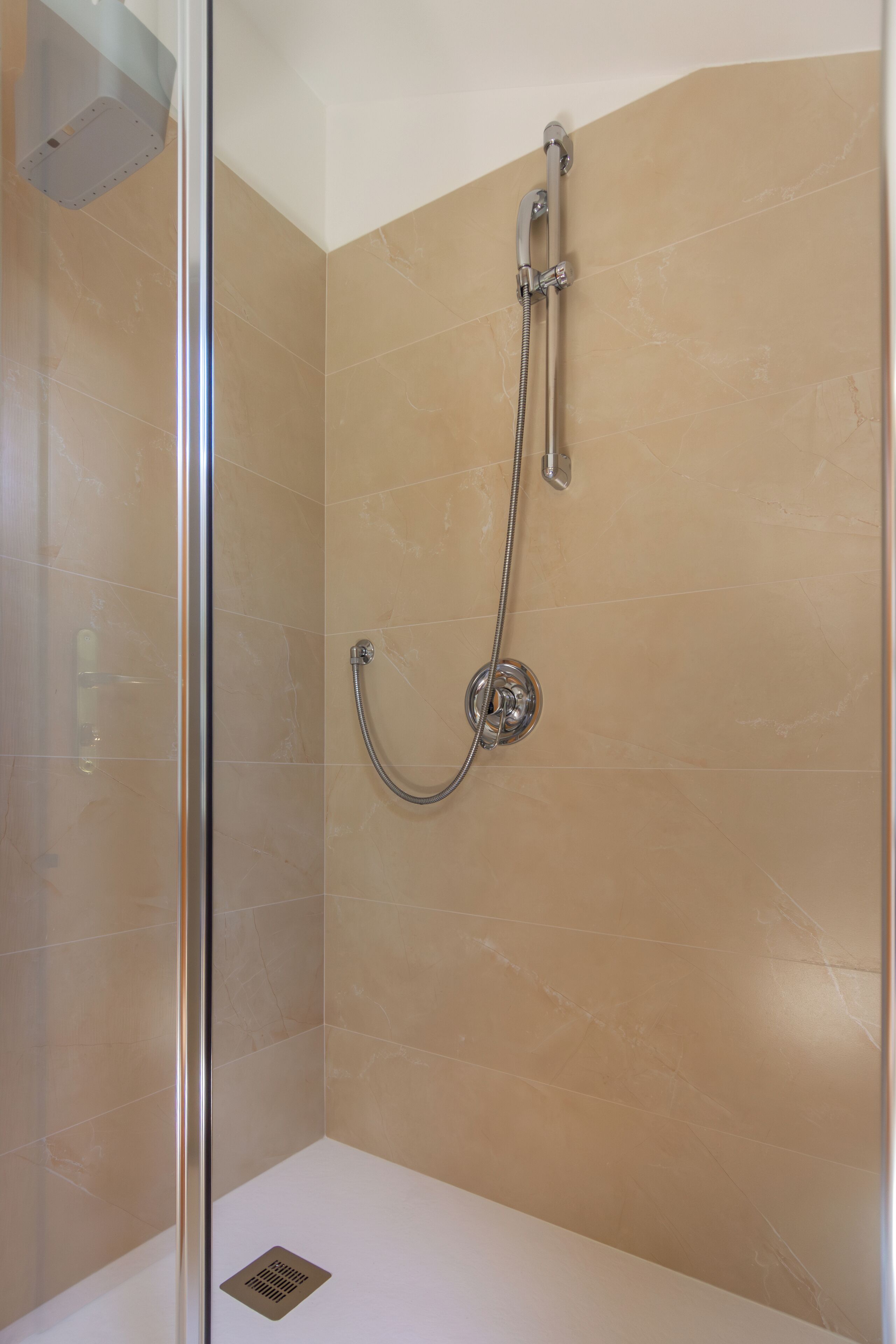 A shower with a glass door, a handheld showerhead, and a wall-mounted faucet.
