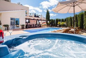 Un bain à remous avec une piscine, un espace extérieur aménagé pour s’asseoir et un coin abrité avec des parasols.